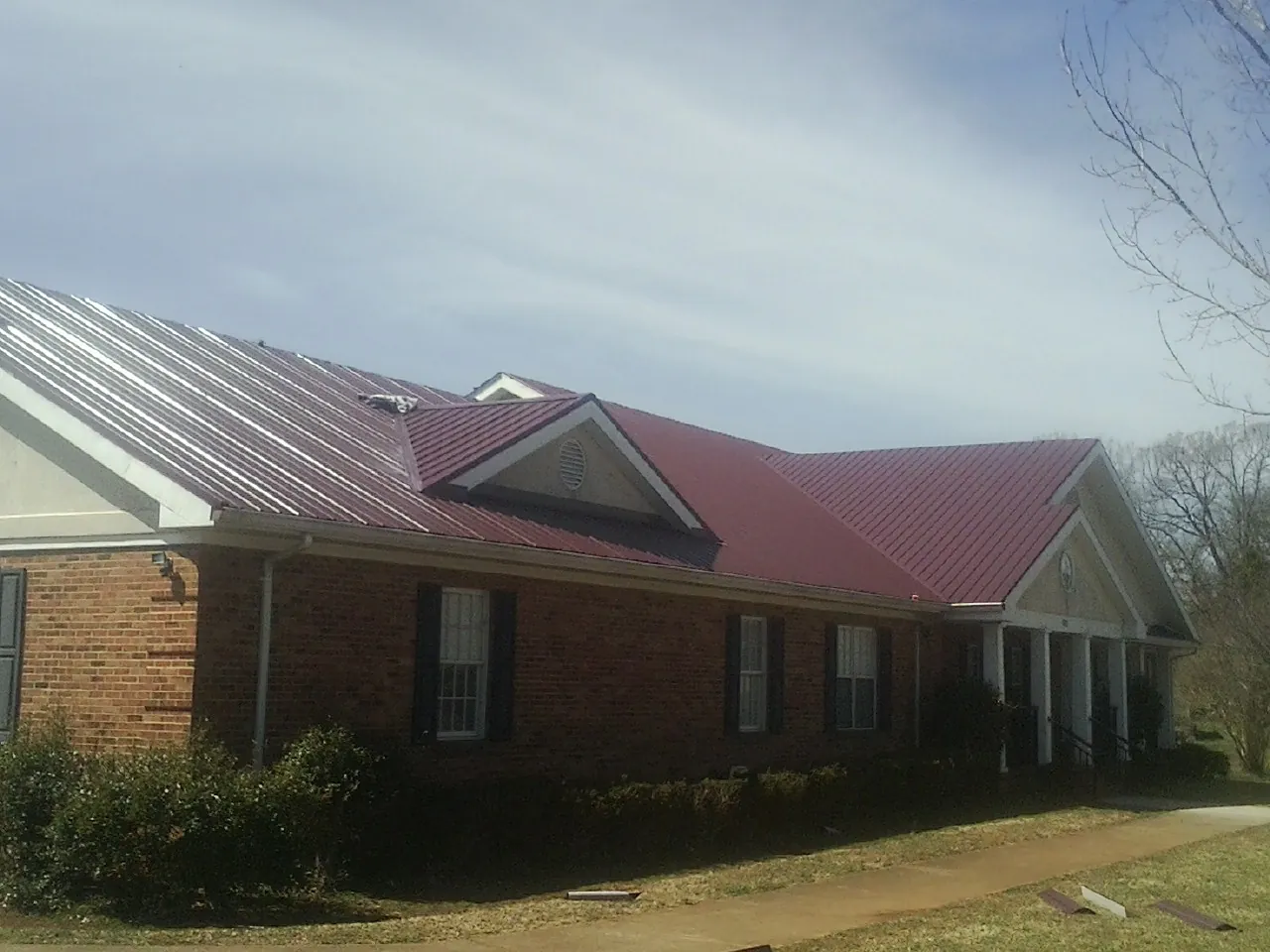 Red metal roof with gabled entries on a long brick building, from a Hail Damage Roof Repair job in Salem